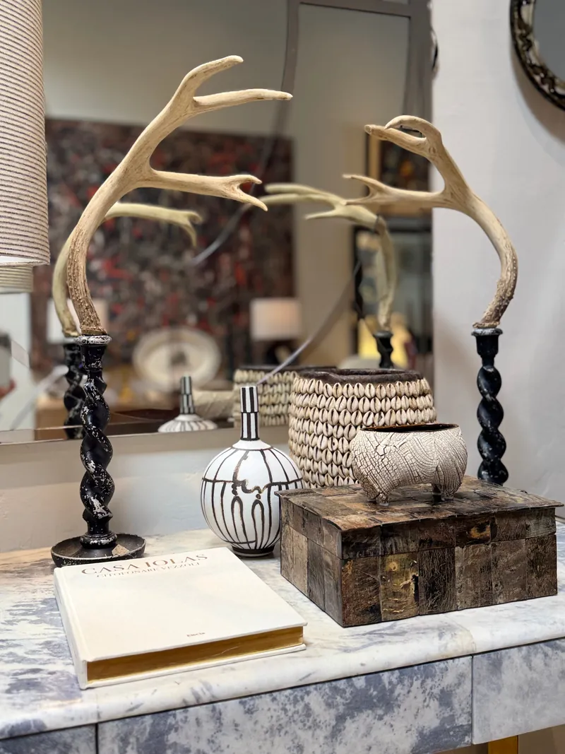 Antler candlesticks on turned blackened wood, a cowrie shell basket, a crackle glazed bowl and a tessellated horn box arranged on a marble console inside THE EDIT