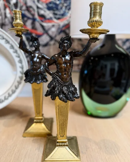 A pair of candlesticks with patinated bronze figures holding fluted candle cups above gilt tapered columns