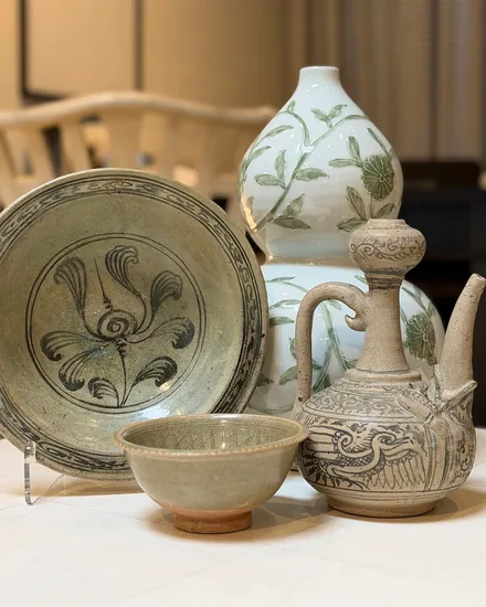 Celadon and stoneware grouped on a pale table: a large painted dish, a small crackle glazed bowl, a green and white gourd vase and a grey ewer