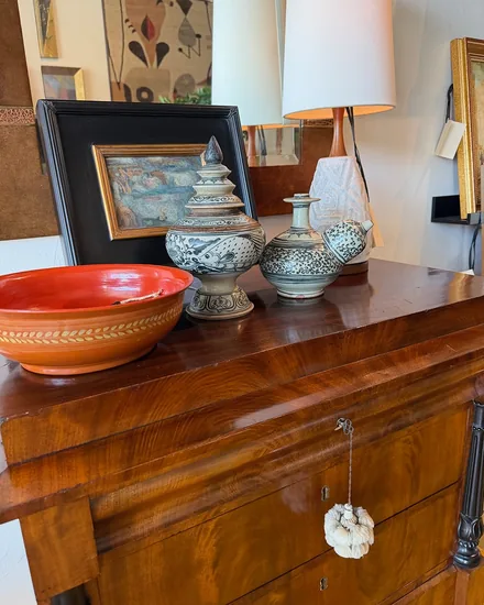 Blue and white painted vessels and an orange glazed bowl on a figured mahogany chest, in front of a framed painting